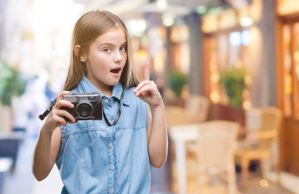 junge schöne Mädchen, die Fotos mit Vintage-Kamera über isolierten Hintergrund überrascht mit einer Idee oder Frage Zeigefinger mit glücklichem Gesicht, Nummer eins - Foto, Bild