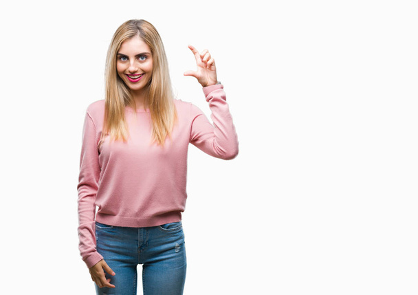 Młody piękny blond kobieta swetrze różowy zima na na białym tle uśmiech i pewność gestem ręką robi znak rozmiar palcami patrząc i aparat. Pojęcie środka. - Zdjęcie, obraz