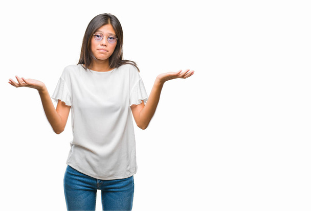 Young asian woman wearing glasses over isolated background clueless and confused expression with arms and hands raised. Doubt concept. - Fotoğraf, Görsel