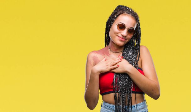 Young braided hair african american with birth mark wearing sunglasses over isolated background smiling with hands on chest with closed eyes and grateful gesture on face. Health concept. - Photo, Image