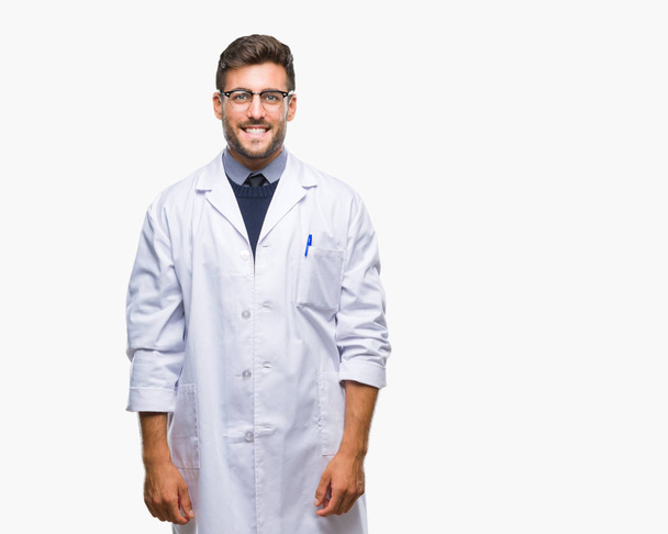 Jonge knappe man dragen arts, scientis vacht over geïsoleerde achtergrond met een gelukkig en cool glimlach op het gezicht. Gelukkig persoon. - Foto, afbeelding
