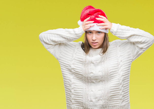 Νέοι όμορφη καυκάσιος γυναίκα φοράει καπέλο Χριστουγέννων πέρα από το απομονωμένο υπόβαθρο που υποφέρουν από πονοκέφαλο, απελπισμένος και τόνισε επειδή τον πόνο και την ημικρανία. Τα χέρια στο κεφάλι. - Φωτογραφία, εικόνα