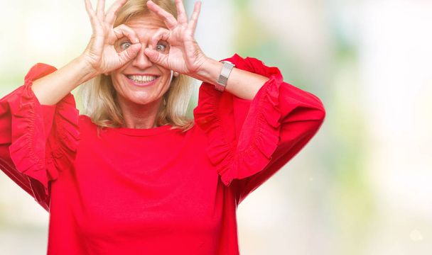 Μέσης ηλικίας ξανθιά γυναίκα απομονωμένη φόντο κάνει εντάξει χειρονομία όπως κιάλια να κολλήσει τη γλώσσα έξω, μάτια αναζητούν μέσα από τα δάχτυλα. Τρελό έκφραση. - Φωτογραφία, εικόνα