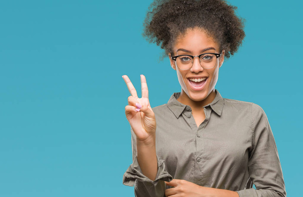 Mladá afro americký žena nosí brýle izolované pozadí usmívající se smajlík, mrkl na fotoaparát dělá znamení vítězství. Číslo dvě. - Fotografie, Obrázek