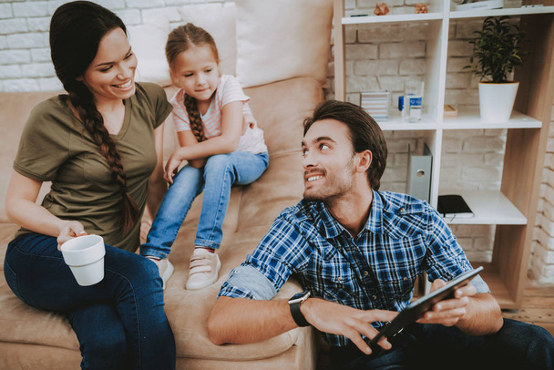 Happy Family. Parents and Daughter. Family Resting Together. Happy Child and Parents. Brown Sofa in Apartment. Man Shows Black Tablet. Smiling Family Resting. Mom with Girl Resting. Look at Father. - Fotoğraf, Görsel