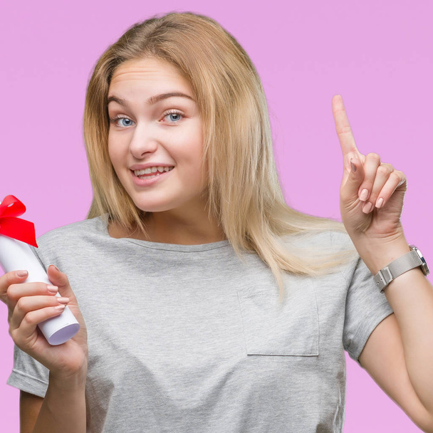 Young caucasian woman holding degree over isolated background surprised with an idea or question pointing finger with happy face, number one - Photo, Image