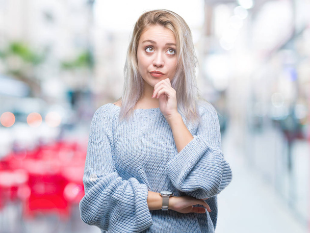 Young blonde woman wearing winter sweater over isolated background with hand on chin thinking about question, pensive expression. Smiling with thoughtful face. Doubt concept. - Photo, Image