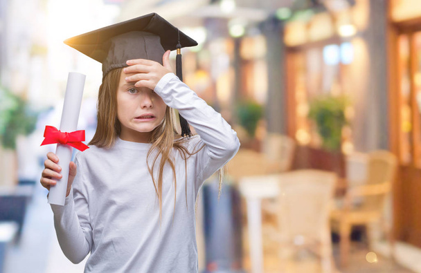 Young beautiful girl wearing graduate cap holding degree over isolated background stressed with hand on head, shocked with shame and surprise face, angry and frustrated. Fear and upset for mistake. - Foto, Bild