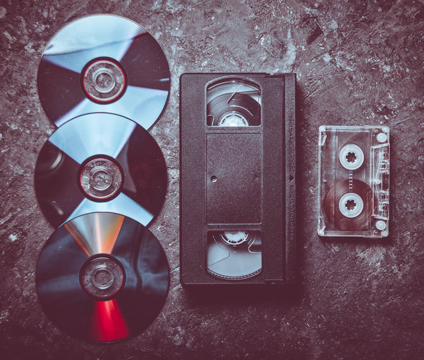 Flach lagen Videokassetten, CDs, Audiokassetten auf einer schwarzen Betonoberfläche. Retro-Medientechnologie der Vergangenheit. Ansicht von oben. - Foto, Bild