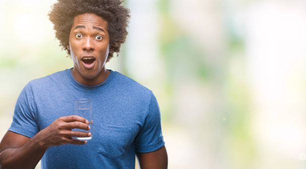 Afro amerikkalainen mies juo lasia vettä yli eristetty tausta peloissaan shokki yllätys kasvot, peloissaan ja innoissaan pelko ilme
 - Valokuva, kuva