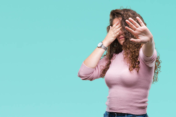 Beautiful brunette curly hair young girl wearing pink sweater over isolated background covering eyes with hands and doing stop gesture with sad and fear expression. Embarrassed and negative concept. - Photo, Image