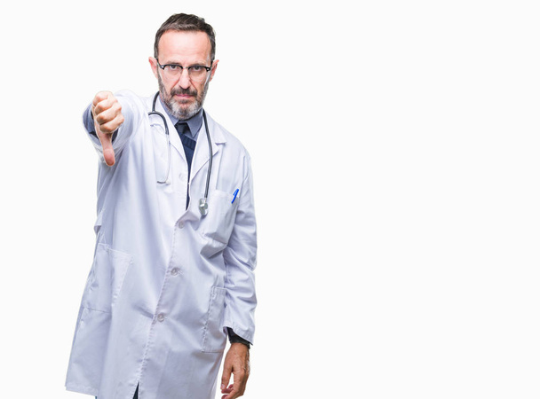 Μέση ηλικία ανώτερος γιατρός γηραιός άνδρας φορώντας ιατρική στολή απομονωμένες φόντο ψάχνει δυστυχισμένοι και θυμωμένος εμφάνιση απόρριψη και αρνητικά με αντίχειρες προς τα κάτω κίνηση. Κακή έκφραση. - Φωτογραφία, εικόνα