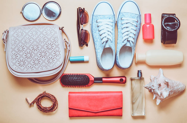 Top view of the girlish spring-summer accessories: sneakers, cosmetics, beauty and hygiene products, bag, sunglasses on a yellow pastel background. Going on a trip. - Photo, Image