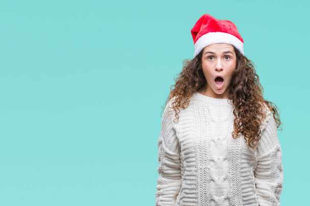 Jeune fille brune portant un chapeau de Noël sur fond isolé effrayé et choqué par l'expression surprise, la peur et le visage excité
. - Photo, image