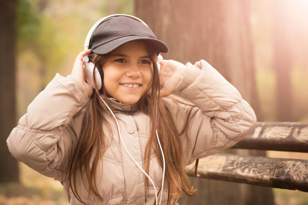 Child girl sitting on a bench in the park and listening to music on headphones.High ISO - Fotoğraf, Görsel