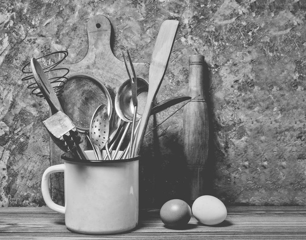 Кухонные инструменты для приготовления пищи на деревянном столе на фоне бетонных стен. Ложка, вилка, деревянная лопатка, скалка, яйца
. - Фото, изображение