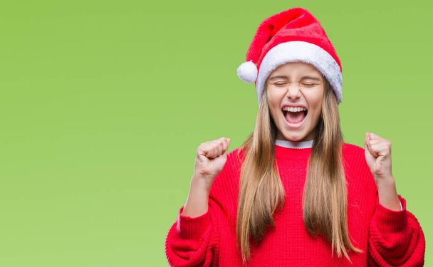Young beautiful girl wearing christmas hat over isolated background excited for success with arms raised celebrating victory smiling. Winner concept. - Φωτογραφία, εικόνα