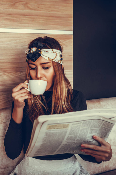 Hermosa joven leyendo el periódico y tomando café mientras usa el portátil por la mañana en la cafetería. Concepto de trabajo de bloguero
 - Foto, imagen