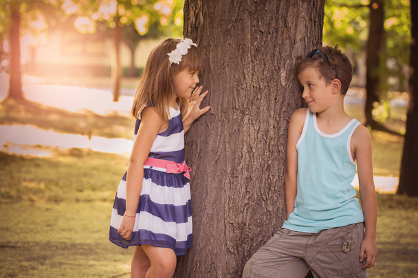 Primer amor. Feliz niño y una niña de pie junto a un árbol en el parque y divertirse. Se miran a los ojos.
 - Foto, imagen