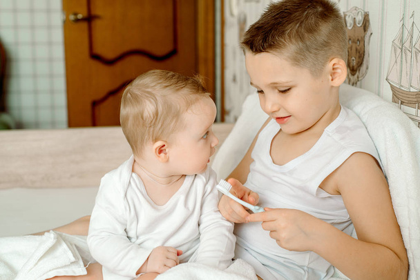 Cute little baby after bathing in a white towel, the girl cleans the first tooth, the boy straightens the polocense. Children after a shower or bath. Concept of health, cleanliness or spa - Фото, зображення