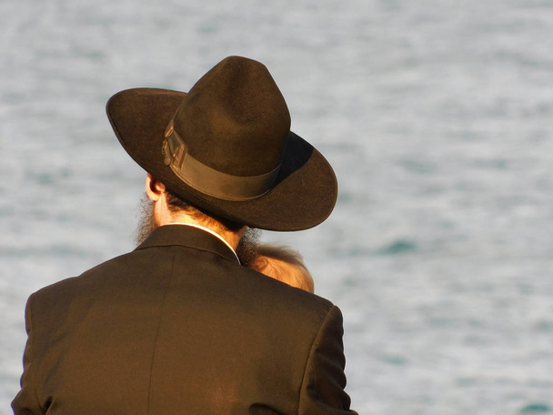 Judío religioso con un niño sentado junto al mar
 - Foto, imagen