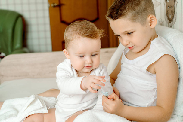Portrait of cute little baby girl with toothbrush. Girl cleans a tooth with a toothbrush. 6 months baby. in a white towel. after shower or bath. Brother helps sister and laughs - Foto, Imagem