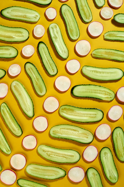 Natural geometric vegetarian pattern with freshly picked vegetables slices of cucumber and radish on a yellow background. Dieting healthy concept. - 写真・画像