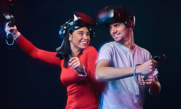 Молода усміхнена пара розважається разом, грає з гарнітурами та контролерами VR
. - Фото, зображення