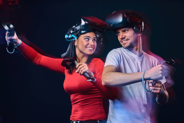Молода усміхнена пара розважається разом, грає з гарнітурами та контролерами VR
. - Фото, зображення
