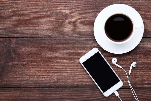Smartphone with earphones and cup of coffee on wooden table - Photo, image
