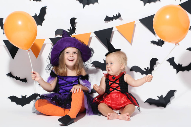 Little girls in halloween costumes with balloons sitting on white background - Фото, изображение