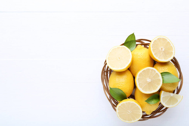 Ripe lemons in basket on white wooden table - Fotoğraf, Görsel