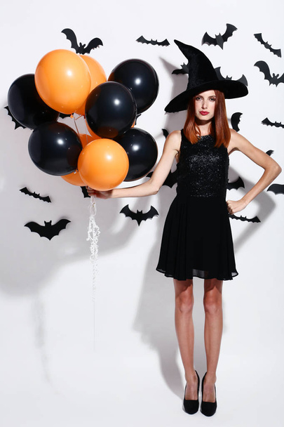 Beautiful redhaired woman with balloons and paper bats on white background - 写真・画像