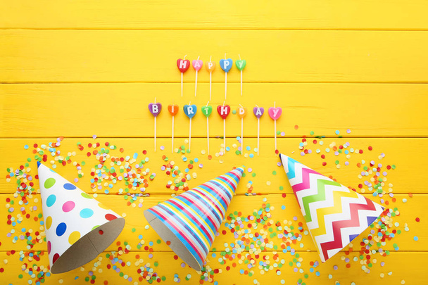 Birthday paper caps with candles and confetti on yellow wooden table - Valokuva, kuva