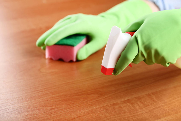 Hands in gloves with sponge and bottle of detergent cleaning kitchen table - Фото, зображення