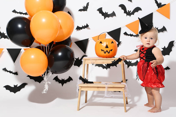 Baby girl in halloween costume with balloons and pumpkin bucket on white background - Foto, Imagem