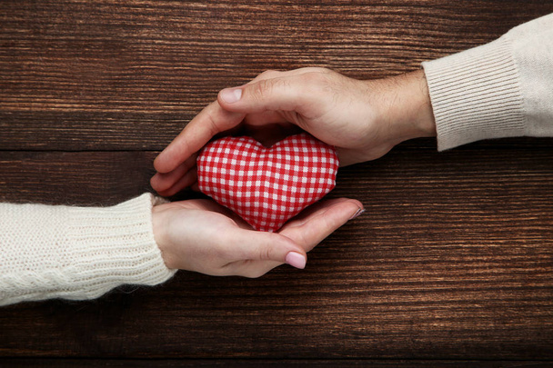 Női és férfi kezében szív piros szövet barna háttér - Fotó, kép