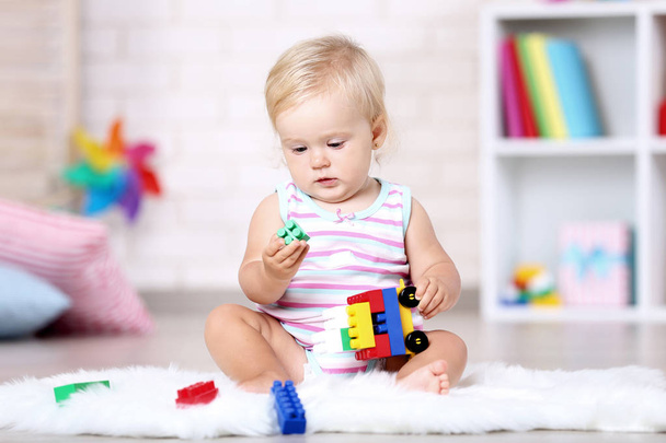 Baby girl sitting on white carpet with toys - Foto, imagen