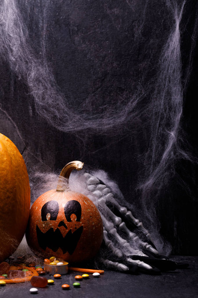 Halloween pumpkin with candles, spiders, web, sweets, horror stories on a dark background, closeup. The concept of autumn holidays. - Photo, image