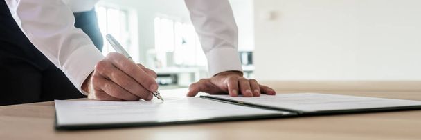 Панорамне зображення бізнесмена, що підписує важливий документ або контракт, стоячи за офісним столом
. - Фото, зображення