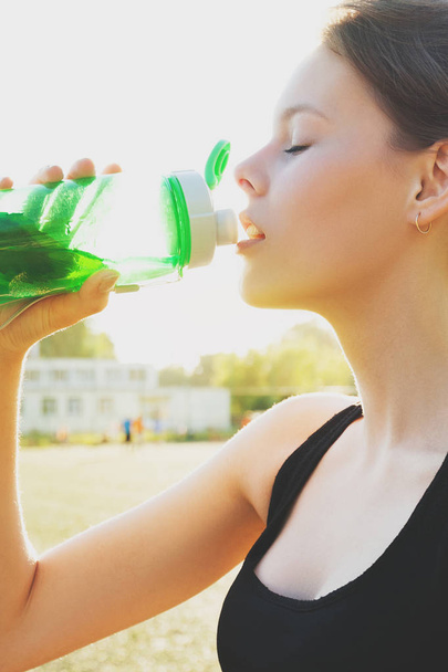 Beautiful young girl is drinking water on sports training. Sports concept - Photo, Image