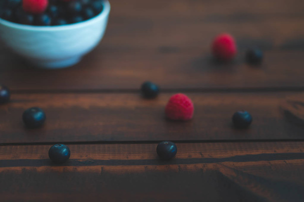 Bowl of blueberries and raspberries on a dark brown table. - Zdjęcie, obraz