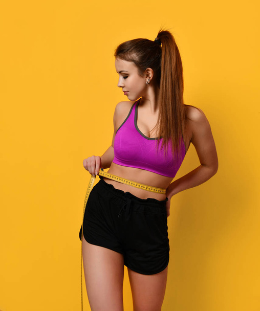 Beautiful sports woman measure her waist with tape measure on yellow background weight loss concept - Fotó, kép