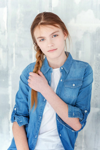 Fiatal boldog aranyos tizenéves lány farmer, farmer kabát és fehér póló ül szürke széket anyagmintás háttér. Alkalmi napi életmód. Iskolás diák és iskolai koncepció - Fotó, kép