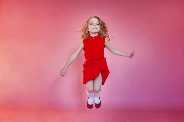 kleine süße lächelnde Mädchen in rotem Kleid springen auf rosa bunte Pastell trendige moderne Mode Pin-up-Hintergrund - Foto, Bild