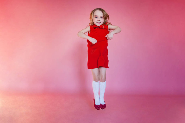 Little cute sweet smiling girl in red dress jumping on pink colourful pastel trendy modern fashion pin-up background - Φωτογραφία, εικόνα