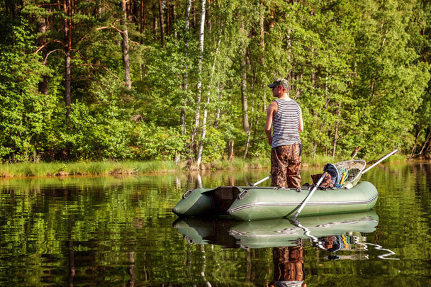 A fisherman is fishing in a boat on a beautiful lake - Фото, изображение