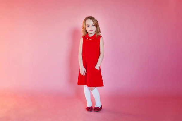 Kis aranyos édes mosolygó lány piros ruhában állt a rózsaszín színes pasztell divatos modern divat pin-up háttér - Fotó, kép