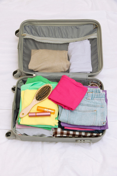 Open grey suitcase with clothing on bed - Foto, imagen