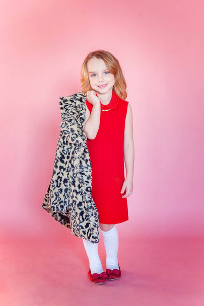 Roztomilý sladký usměvavá holčička v červených šatech, stojící na pozadí pin-up růžové barevné pastelové trendy moderní módy - Fotografie, Obrázek